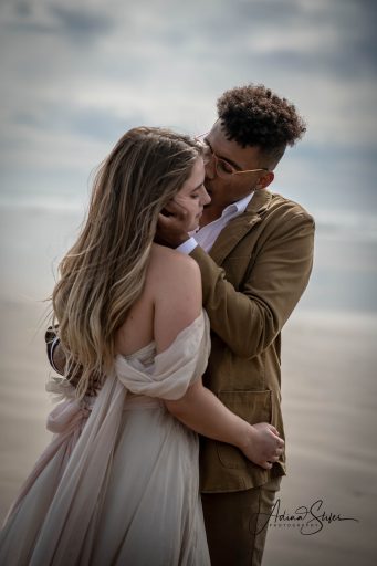 black groom holds his white wife's face and gently kisses her on the beach during their seattle wedding with adina stiles photography