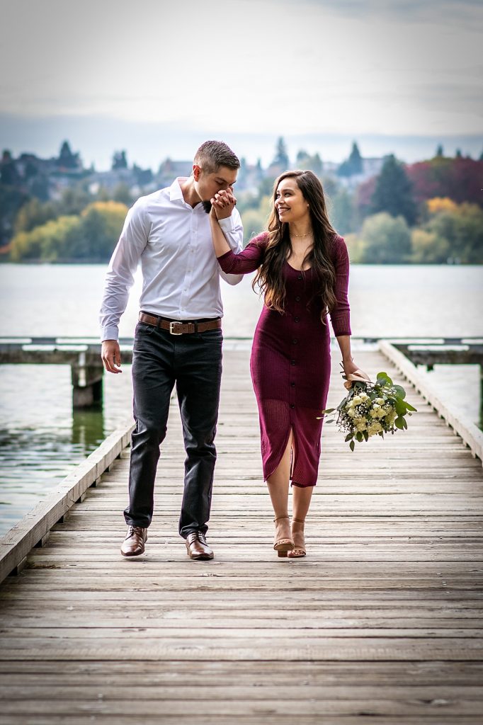 A handsome man kisses his partner's hand as they walk together during a photoshoot in Green Lake Park, Seattle.