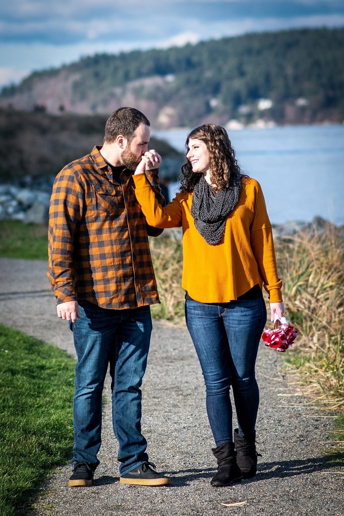 A man kisses his finace's hand while taking engagement photos at Point Defiance Park, Tacoma, a beautiful photo spot in Puget Sound.