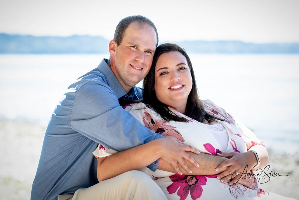 A couple sits on the beach together, smiling, at Seahurst Park in Burien for a Puget Sound photo session.