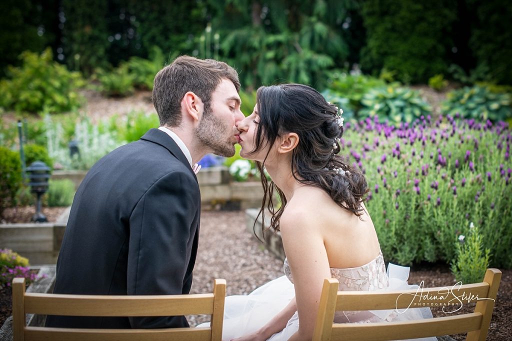 A newlywed couple kisses in front of beautiful gardens during their wedding Willows Lodge in Woodinville while Puget Sound wedding photographer Adina Stiles captures the moment.