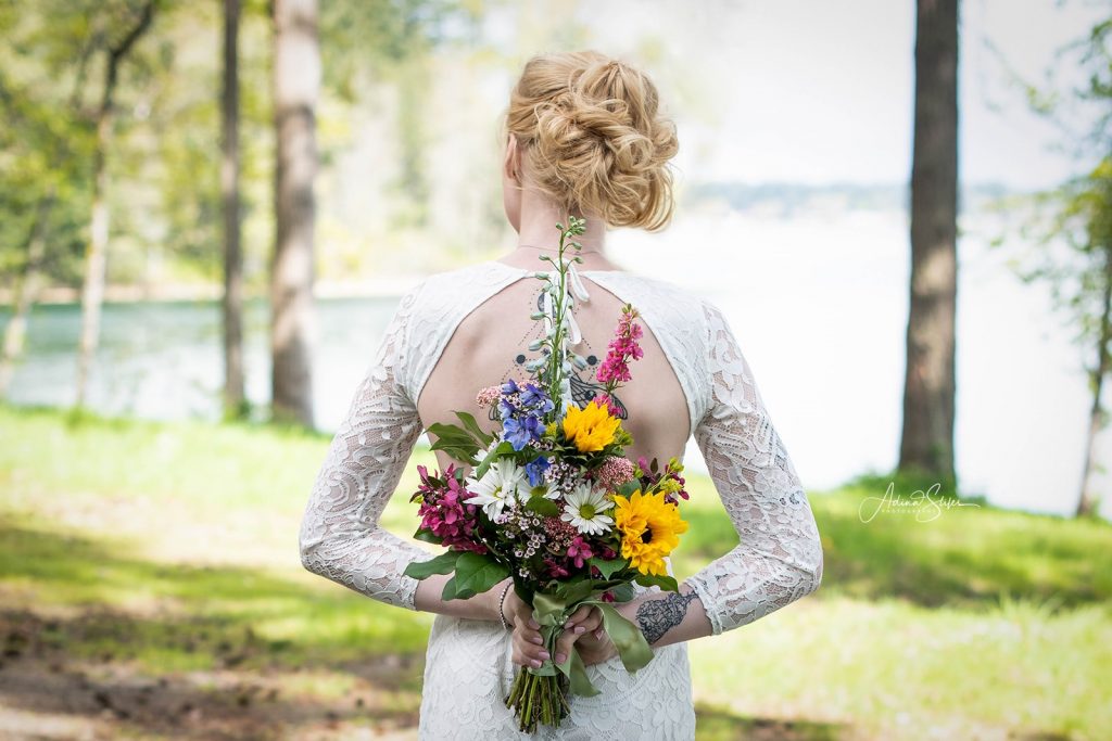A bride holds a colorful bouquet behind her back during an intimate wedding in Maple Valley, Washington.